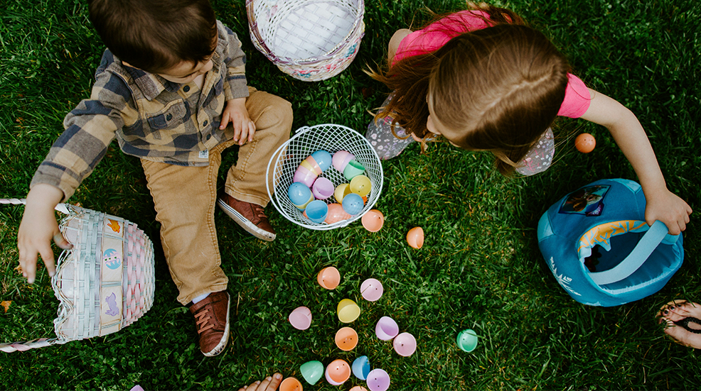 Birds eye view of children sitting on grass, filling baskets with easter eggs